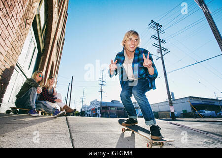Frauen, die gerade Mann Skateboarden auf städtischen Bürgersteig Stockfoto