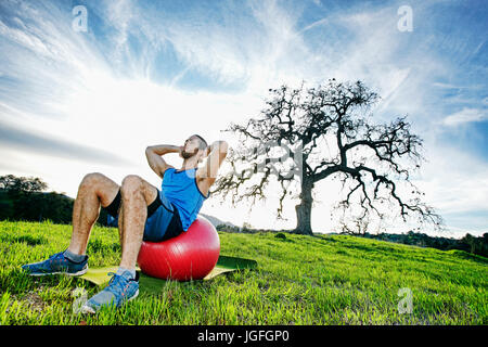 Kaukasischen Mann Sit auf Fitness-Ball im Feld in der Nähe von Baum Stockfoto