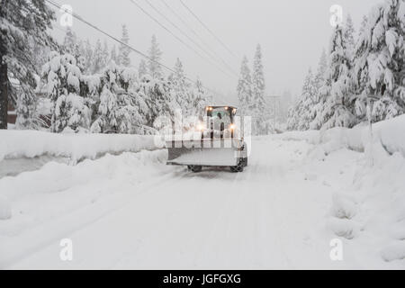 Traktor mit Schneepflug fahren auf remote-Straße Stockfoto