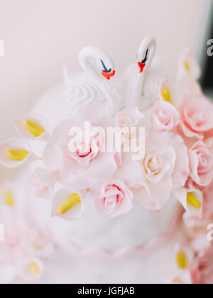 Die kleine Schwäne schmücken die weiße Hochzeitstorte mit rosa Blüten. Stockfoto