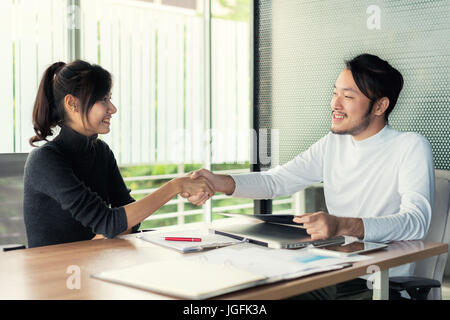 Paar asiatische Geschäftsleute mit Freizeitkleidung im Gespräch mit glücklich und zitternder Hand in modernen Büros oder im Café. Business-Erfolg-Konzept