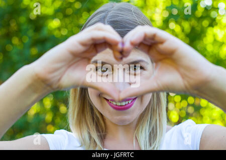 Bild von eine fröhliche junge Frau, die ein Herz mit Hände heraus lugen Outdoor Stockfoto