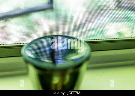 Reflexion des Netzes Fenster- und grünen Laub in Wasser oder Tee auf Fensterbank Stockfoto