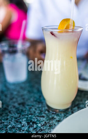 Makro Nahaufnahme von Pina Colada mit Zitrone im Glas mit Strohhalm auf Tisch Stockfoto