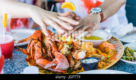 Makro Nahaufnahme von Hummer und Fisch auf Teller mit Sauce Tartar und Knoblauchbutter und zwei Hände Stockfoto