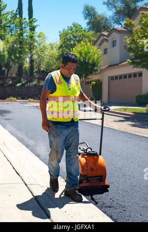 Ein Mitarbeiter des amerikanischen Asphalt zieht eine manuelle Müllpresse über eine neu angelegte Straßenoberfläche während einer Straßenbau und resurfacing Projekt im Stadtteil San Francisco Bay Area von San Ramon, Kalifornien, 26. Juni 2017. Stockfoto