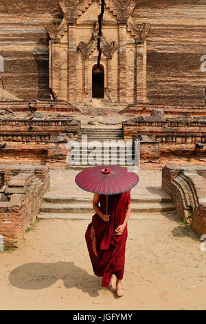 Ein buddhistischer Mönch in der roten Robe mit Regenschirm stehen die zerstörten Pagode. Stockfoto