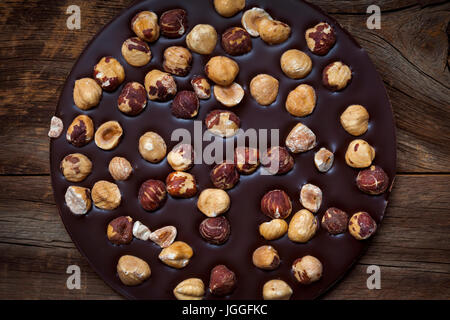 Runde handwerklichen dunkle Schokolade mit ganzen Haselnüssen auf rustikalen Holz Hintergrund, Draufsicht Stockfoto
