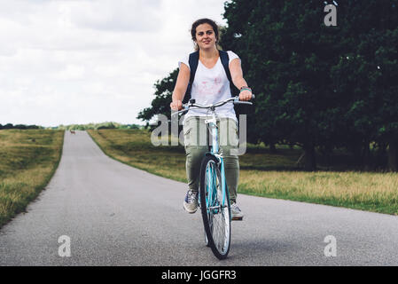 Lächelnd hübsche junge Frau Reiten Fahrrad in einem Land unterwegs im park Stockfoto