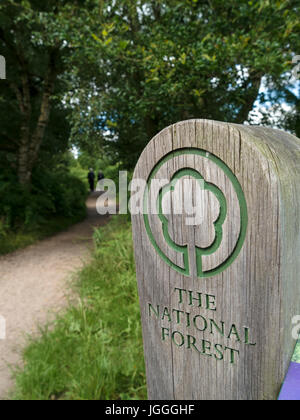 Holzschild und fernen Spaziergänger im Wald Wanderweg auf der National Forest Weg, Derbyshire, England, UK Stockfoto