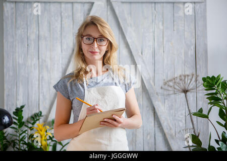 Frau Blumengeschäft mit Brille und Schürze mit Notebook in Händen. Floristik-Konzept Stockfoto