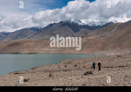 Xinjiang, China - 15. August 2012: Zwei uigurische Frauen zu Fuß durch einen See mit den Bergen im Hintergrund, auf dem Karakorum Highway, im nordwestlichen C Stockfoto