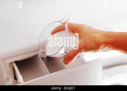 Hand der Frau, das Waschmittel in der Waschmaschine füllt Stockfoto
