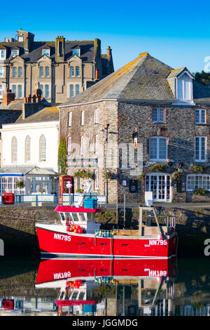 Einen warmen und ruhigen Sommer Morgen im malerischen Fischerdorf Dorf von Padsow in Cornwall, England mit leuchtend roten Fischerboot gegen Hafenmauer Stockfoto