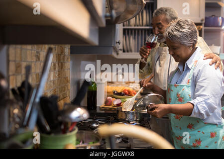 Mann mit Wein, während die Frau, die Zubereitung von Speisen in der Küche zu Hause Stockfoto