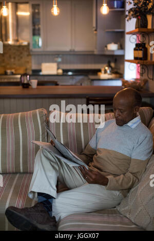 Mann liest Zeitung sitzend auf Sofa im Wohnzimmer zu Hause Stockfoto