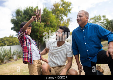 Jungen zeigen Spielzeugflugzeug Vater hockend von senior woman in Hof Stockfoto