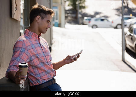 Seitenansicht der junger Mann mit Handy und stützte sich auf Wand Stockfoto