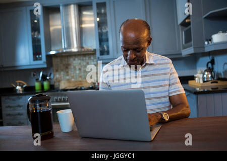 Ältere Mann mit Laptop am Tisch in der Küche zu Hause Stockfoto