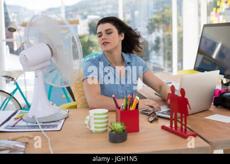 Weibliche executive genießen Brise vom Tischventilator im Büro Stockfoto