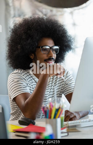 Junger Mann mit lockigem Haar über Computer in Kreativbüro Stockfoto