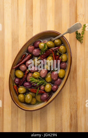 Draufsicht der Oliven mit Chili-Paprika und Kräuter im Container auf Schneidebrett Stockfoto