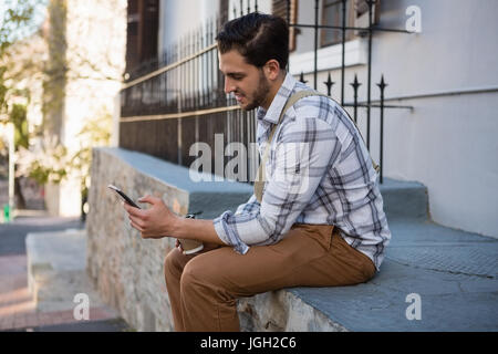 Seitenansicht der Mann mit Handy auf Stützmauer sitzend Stockfoto