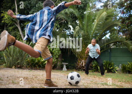 Jungen Fußball spielen mit Großvater auf Feld in Hof Stockfoto