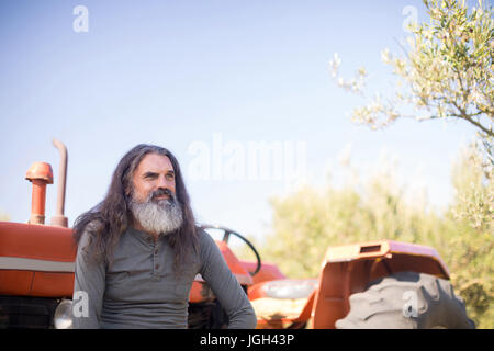 Nachdenklicher Mann sitzen gegen Traktor in Olive Farm an einem sonnigen Tag Stockfoto