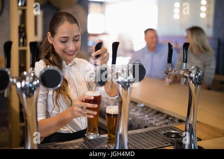 Lächelnd weiblichen Barkeeper Füllung Bier aus bar Pumpe am Tresen Stockfoto