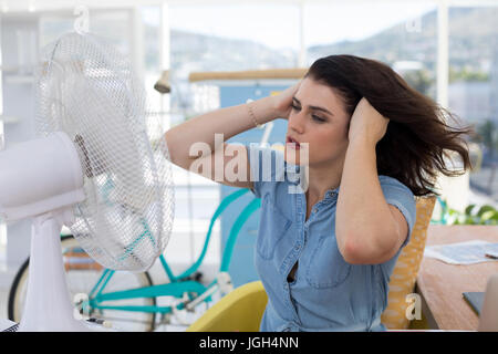 Weibliche executive genießen Brise vom Tischventilator im Büro Stockfoto