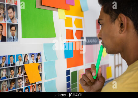 Nachdenklicher junger Mann, Blick auf Haftnotizen in Kreativbüro Stockfoto