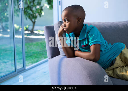 Nachdenkliche junge wegsehen beim Sitzen auf dem Sofa zu Hause Stockfoto