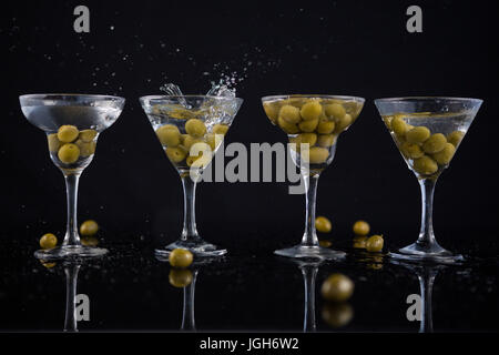 Nahaufnahme von Oliven planschen im zu einem cocktail Martini mit Kalk auf Tisch vor schwarzem Hintergrund Stockfoto