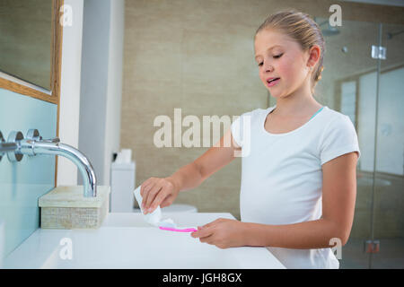 Mädchen, die Zahnpasta auf die Bürste stehend mit Waschbecken im Bad entfernen Stockfoto