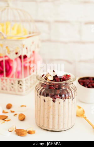 Über Nacht Chia Pudding mit Chia-Samen, Hafer, Granatapfel und Kokos-Chips. Gesundes Frühstück-Konzept. Hellen Ziegel Wand Hintergrund. Gelbe Rosen in Stockfoto