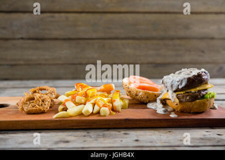 Nahaufnahme von Pommes Frites mit Sauce und Burger und Zwiebel Ringe auf Schneidebrett Stockfoto