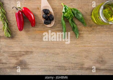 Nahaufnahme von getrockneten Oliven, frische Kräuter mit Olivenöl und rote Chilis auf Tisch Stockfoto