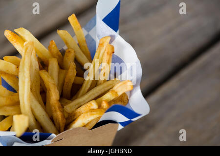 Nahaufnahme von Pommes Frites mit Wachspapier im Container auf Tisch Stockfoto