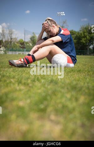 Volle Länge des frustrierten weibliche Fußballspieler sitzen auf Feld an sonnigen Tag Stockfoto