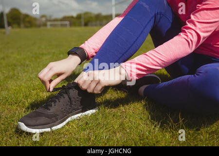 Geringen Teil der Sportlerin, die Schnürsenkel zu binden, beim Sitzen auf der Wiese Stockfoto