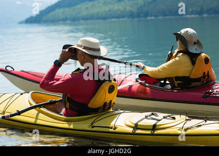 Mann mit dem Fernglas während Kajak mit Frau im See an sonnigen Tag Stockfoto