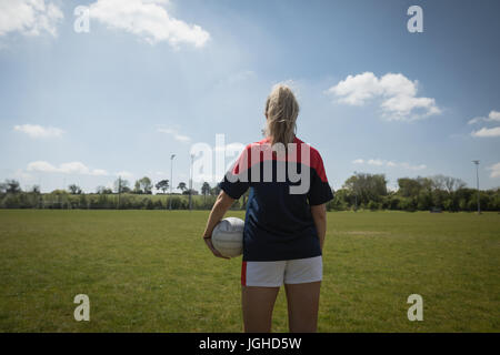 Rückansicht des weiblichen Fußballspieler mit Ball stehend auf Feld gegen Himmel Stockfoto