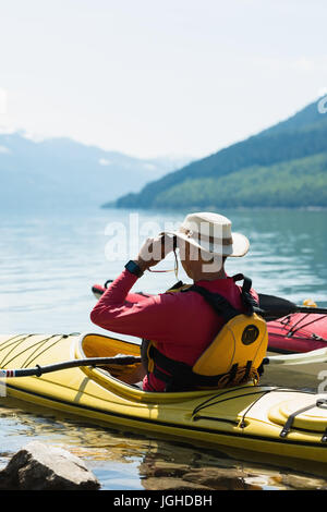 Mann mit dem Fernglas beim Sitzen im Kajak auf See gegen Himmel Stockfoto