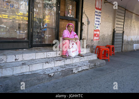 Eine südasiatische Frau in ethnischen Kleid hält für eine Rast nach dem Einkauf. Auf 73rd Street in Jackson Heights, Queens, New York. Stockfoto