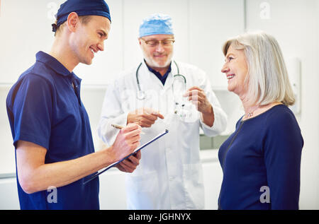 Senior Medic Beratung Erwachsene Patientin während junge lächelnde Assistentin stehend und schreiben in Tablettenform. Stockfoto