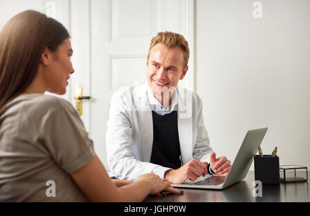 Professionelle Kosmetiker Mann am Laptop im Büro zu sitzen und Beratung junge Frau. Stockfoto