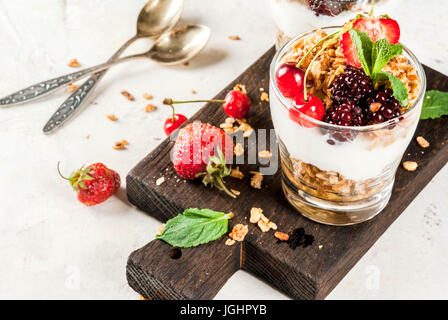 Gesundes Frühstück. Sommer Beeren und Früchte. Hausgemachte griechische Joghurt mit Müsli, Brombeeren, Erdbeeren, Kirschen und Minze. Auf weißem Beton st Stockfoto