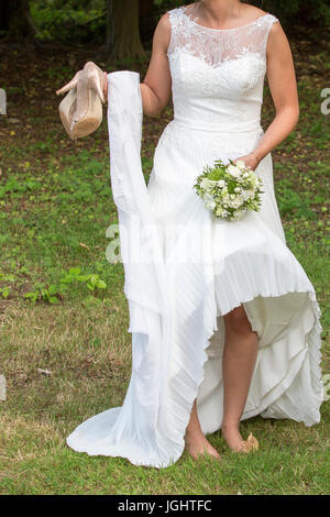 Braut mit Schuhen in der Hand und grün und weiß Bouquet in der anderen Hand barfuß Stockfoto