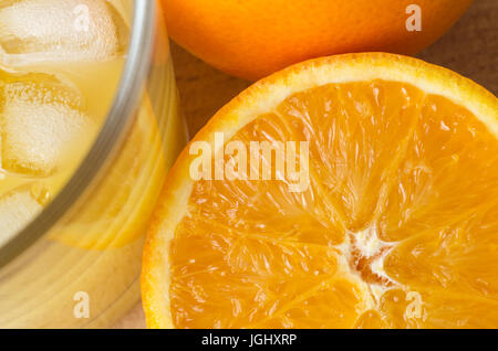 Overhead hautnah Ernte Schuss Orangensaft mit Eiswürfeln, einem geschnittenen Halbjahr eine Orange und eine ganze Orange mit Schale intakt. Stockfoto